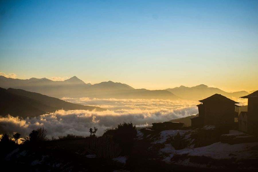 Sunrise over Himalayan mountain silhouettes with sea of clouds and traditional lodge